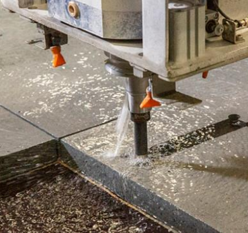 Ein Prüfkörper oder Probezylinder wird zur Prüfung der Konsistenz oder Verdichtung aus dem Beton herausgezogen. Der graue, zähflüssige Carbonbeton ist in einem zylindrischen Behälter enthalten, während ein Mitarbeiter in Schutzkleidung und Handschuhen den Prüfkörper vorsichtig herauszieht. Die Szene spielt in einer industriellen Umgebung, möglicherweise in einem Labor oder einer Produktionshalle, mit unscharfem Hintergrund, der die Aufmerksamkeit auf die Aktion des Mitarbeiters und den Betonprüfkörper lenkt.